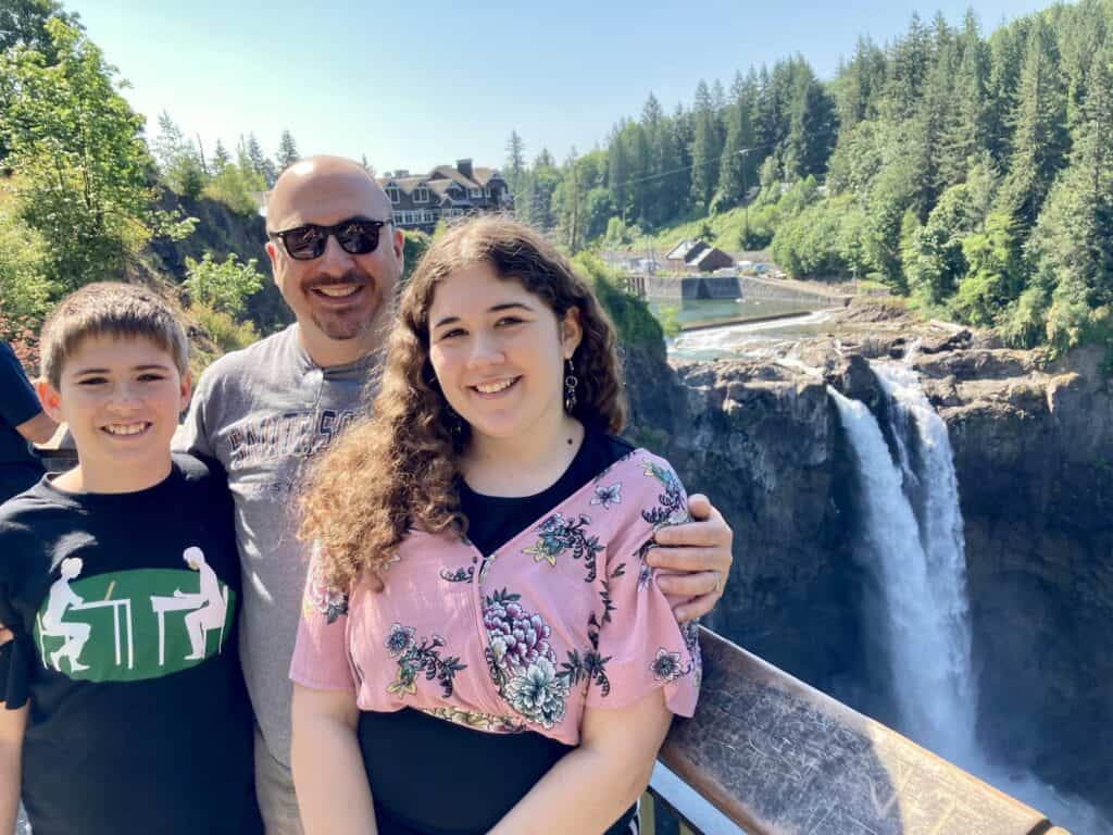 A man, a girl, and a boy stand in front of Snoqualmie Falls