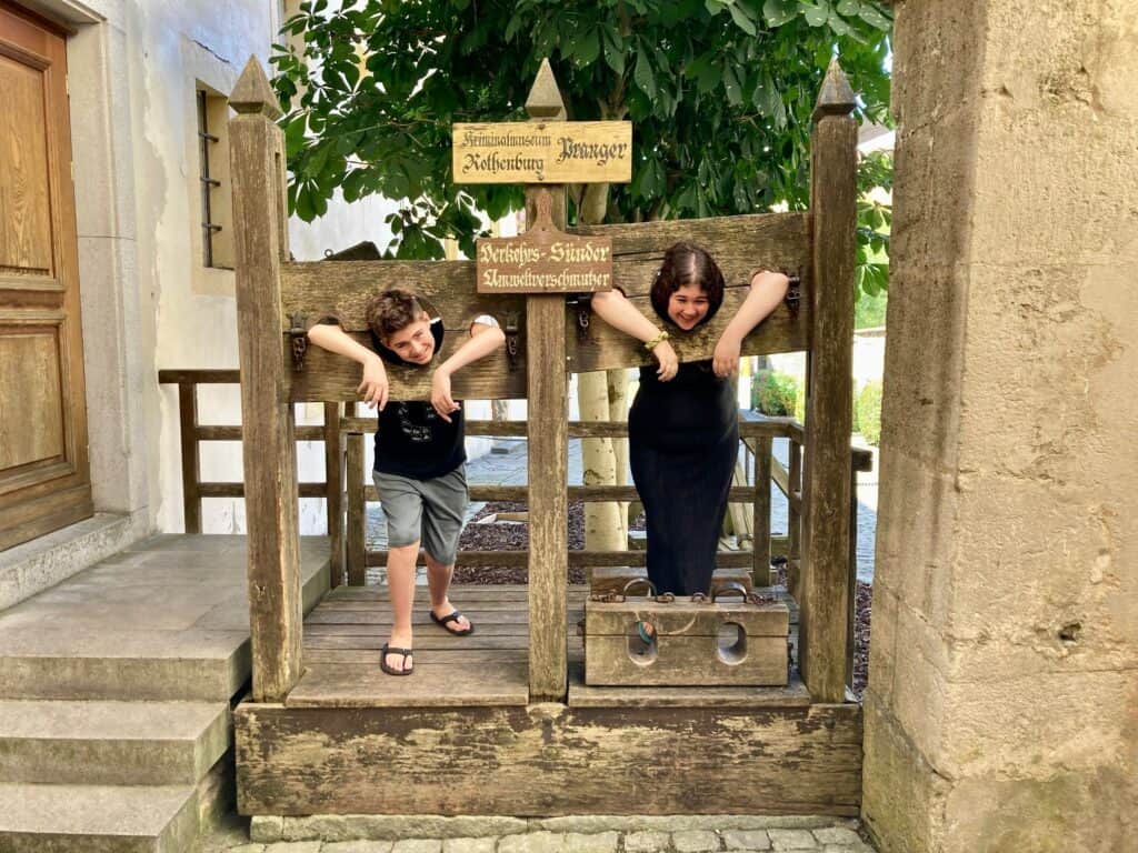 A boy and a girl posing in stocks outside Medieval Crime Museum in Rotheburg ob der Tauber, Germany