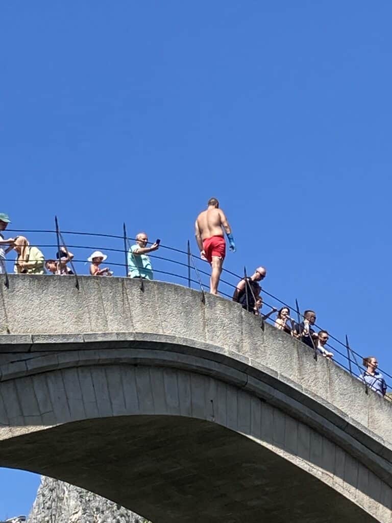 A man stands on the edge of Stari Most Bridge, collecting tips before jumping