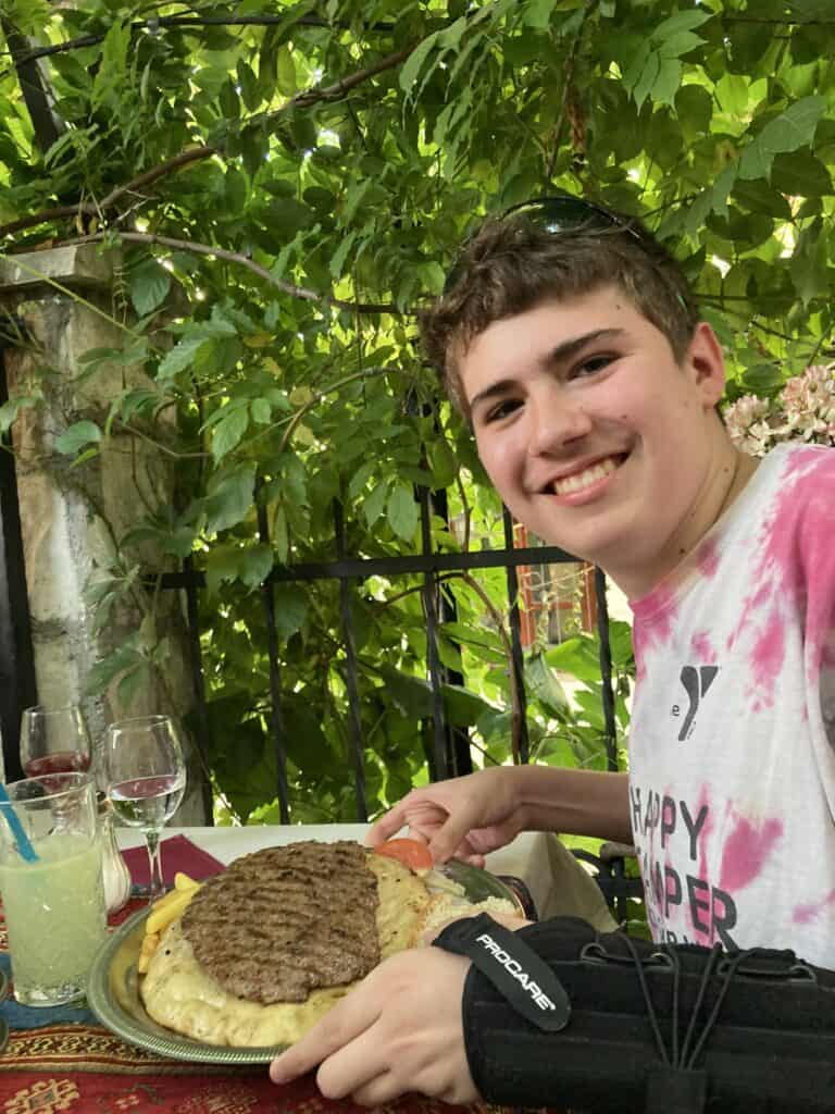 A boy holding a piece of beef on a piece of bread, in Mostar, Bosnia and Herzegovina