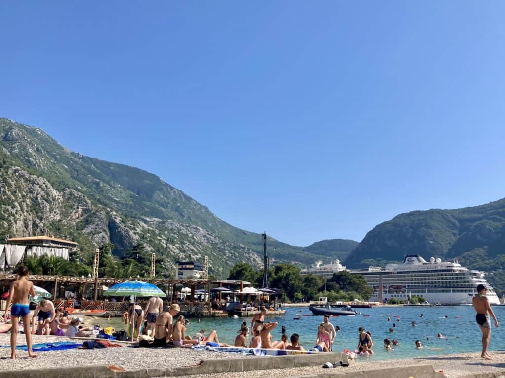 Cruise ship in the bay of Kotor, there are people on the beach in the foreground