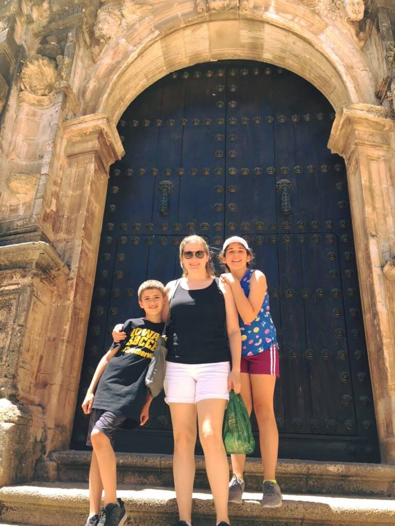 Woman and two children in front of a large door in Spain