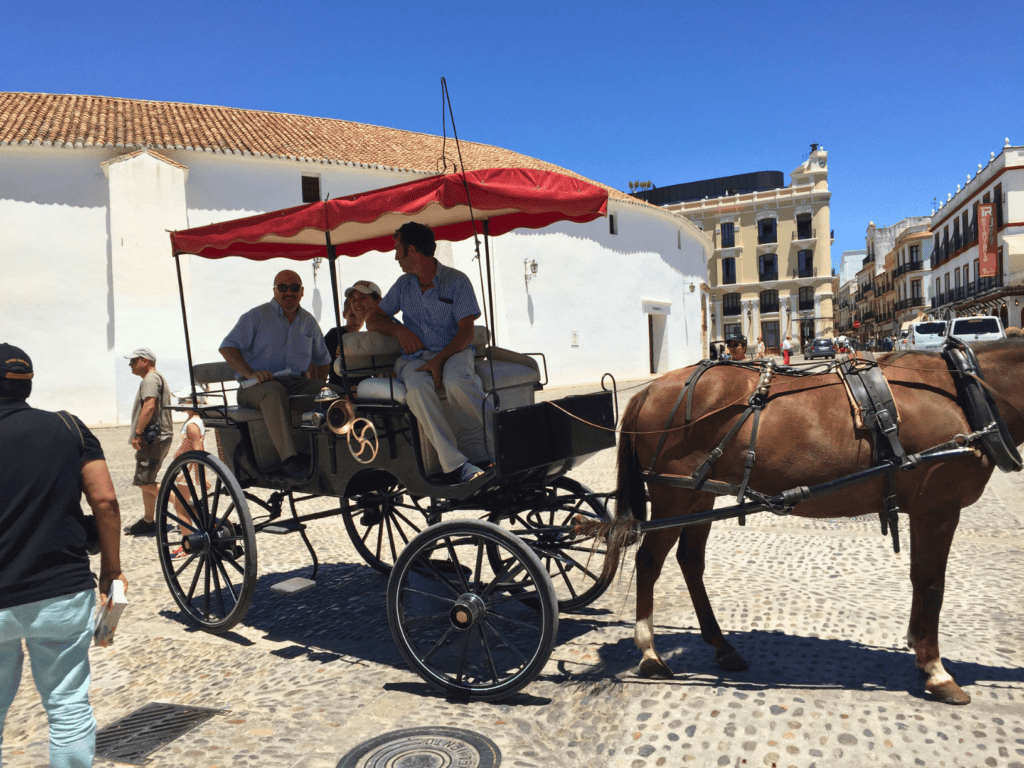 Two men and two children in a cart pulled by a horse outside of a bullring in Spain