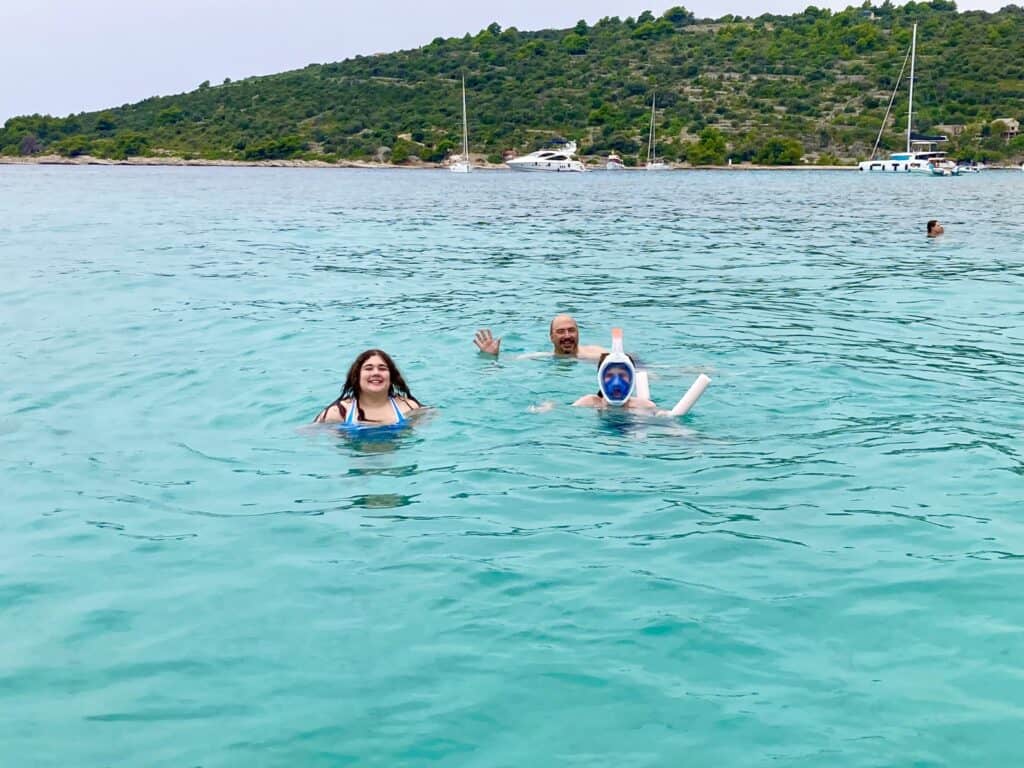 A teen girl and boy and a man swim in blue water in Split, Croatia