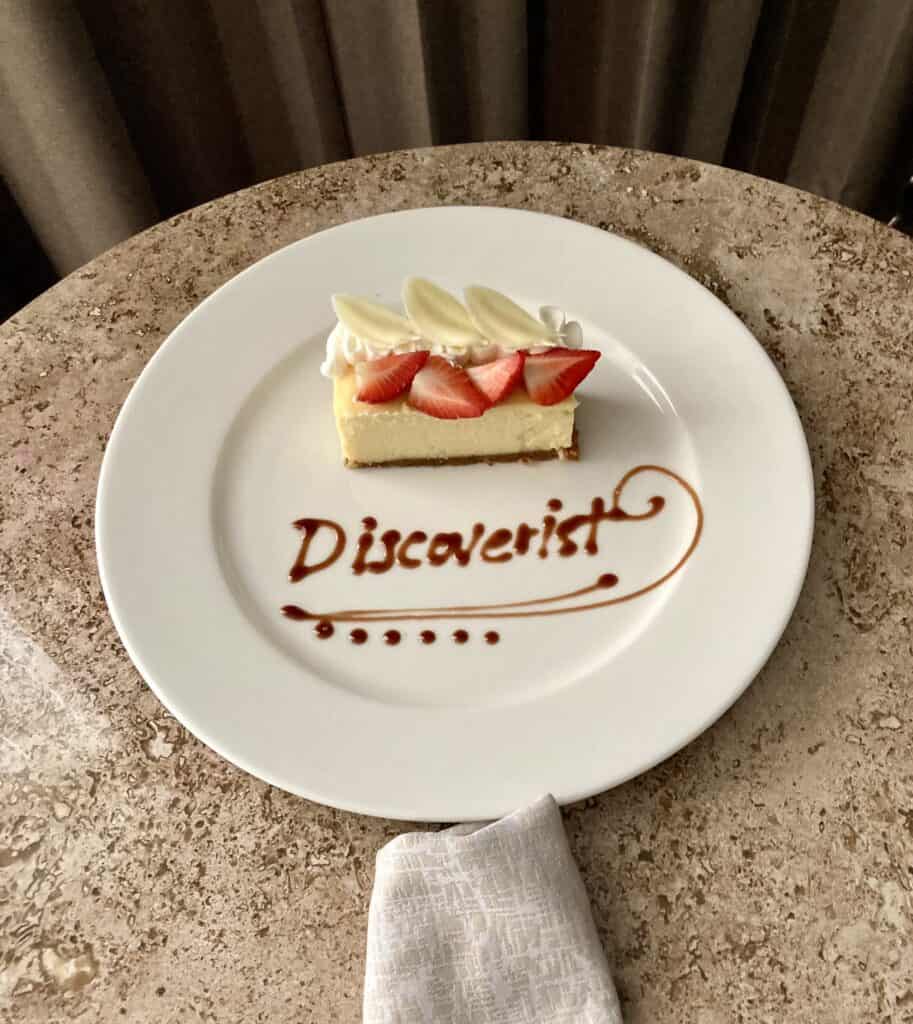 Piece of cheesecake on a plate, topped with strawberries. The word "Discoverist" is written on the plate.