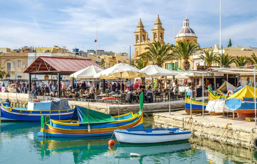 Colorful boats in front of an outdoor restaurant next to the sea in Malta